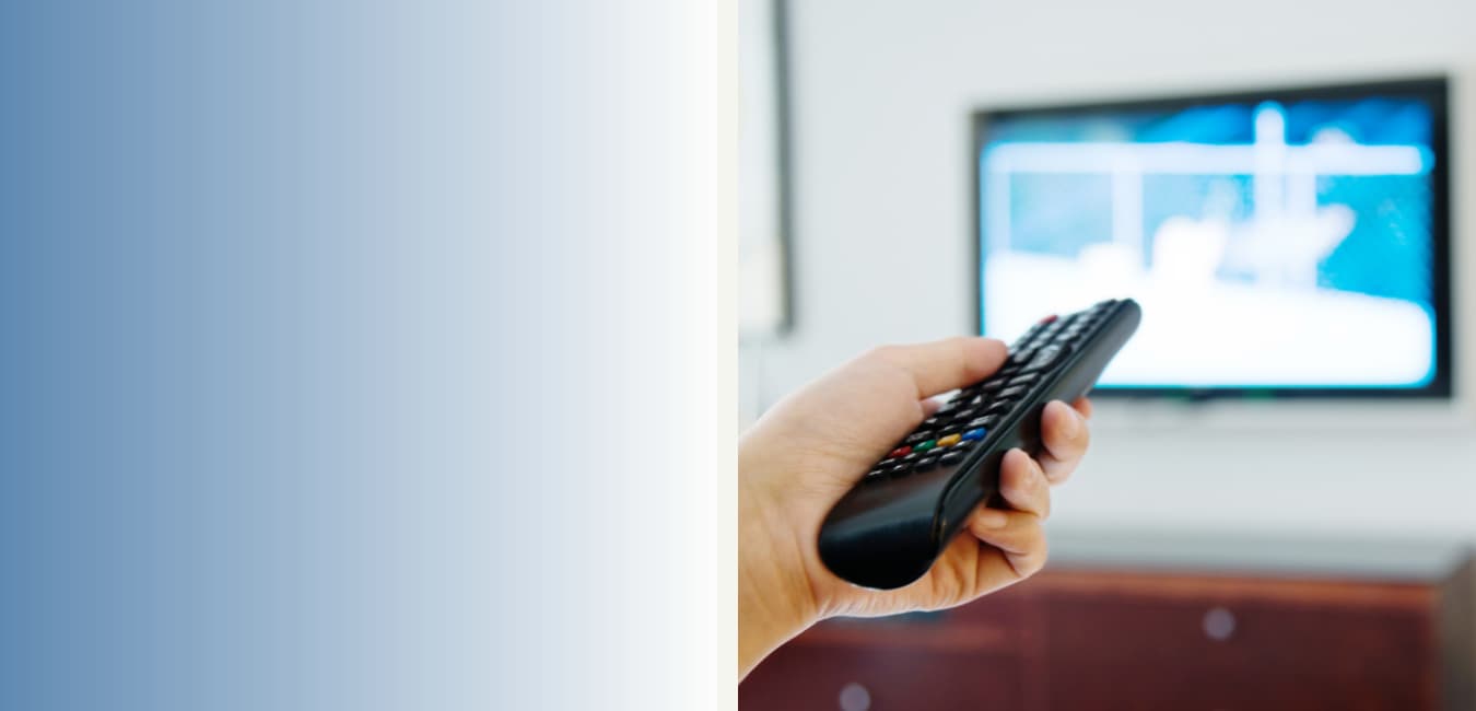 Hand with remote control pointing at wall-mounted TV